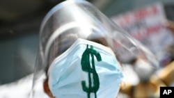 Una trabajadora de la salud usa doble protección. Su mascarilla está marcada con un signo de dólar en apoyo de la dolarización, participa en una protesta por el Primero de Mayo, o Día Internacional de los Trabajadores, en Caracas.