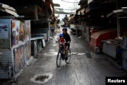 A woman rides a bicycle with her child in a closed market after Israel imposed a second nationwide coronavirus disease (COVID-19) lockdown amid a rise in infections in Tel Aviv, Israel, Sept. 25, 2020.