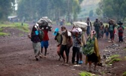 FILE - Civilians displaced by recent fighting between Congolese army and M23 rebels carry their belongings as they walk along a road in Munigi village near Goma in the eastern Democratic Republic of Congo, Sept 1, 2013.