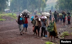 FILE - Civilians displaced by recent fighting between Congolese army and M23 rebels carry their belongings as they walk along a road in Munigi village near Goma in the eastern Democratic Republic of Congo, Sept 1, 2013.