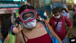 Una mujer usa una máscara de buceo y una máscara quirúrgica como precaución contra la propagación del nuevo coronavirus, mientras compra alimentos en un mercado popular en Lima, Perú.