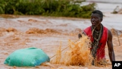 FILE - A man pulls his luggage while trying to cross a road damaged by El Niño rains in Tula, Tana River county in Kenya on Saturday, Nov. 25, 2023. 