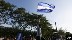 Un manifestante enmascarado sostiene una bandera nacional de Nicaragua durante una manifestación de protesta por la represión del gobierno y un llamado a la paz, en Managua, Nicaragua, el lunes 23 de abril de 2018.