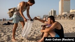 Julian Mercer mengumpulkan puntung rokok dari seorang pengunjung di pantai Tel Aviv, Israel, 20 April 2021. (Foto: Amir Cohen/REuters)