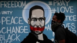 FILE - A man with a face covering walks past a mural depicting George Floyd during a protest in Los Angeles, May 31, 2020.