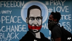 FILE - A man walks past a mural depicting George Floyd during a protest in Los Angeles, May 31, 2020.