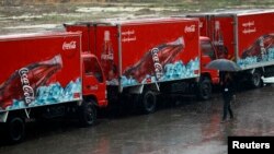 A woman walks near Coca-Cola vehicles during rainfall in Yangon, Myanmar, June 4, 2013.