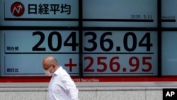 A man wearing a face mask walks past an electronic stock board showing Japan's Nikkei 225 index at a securities firm in Tokyo Monday, May 11, 2020.