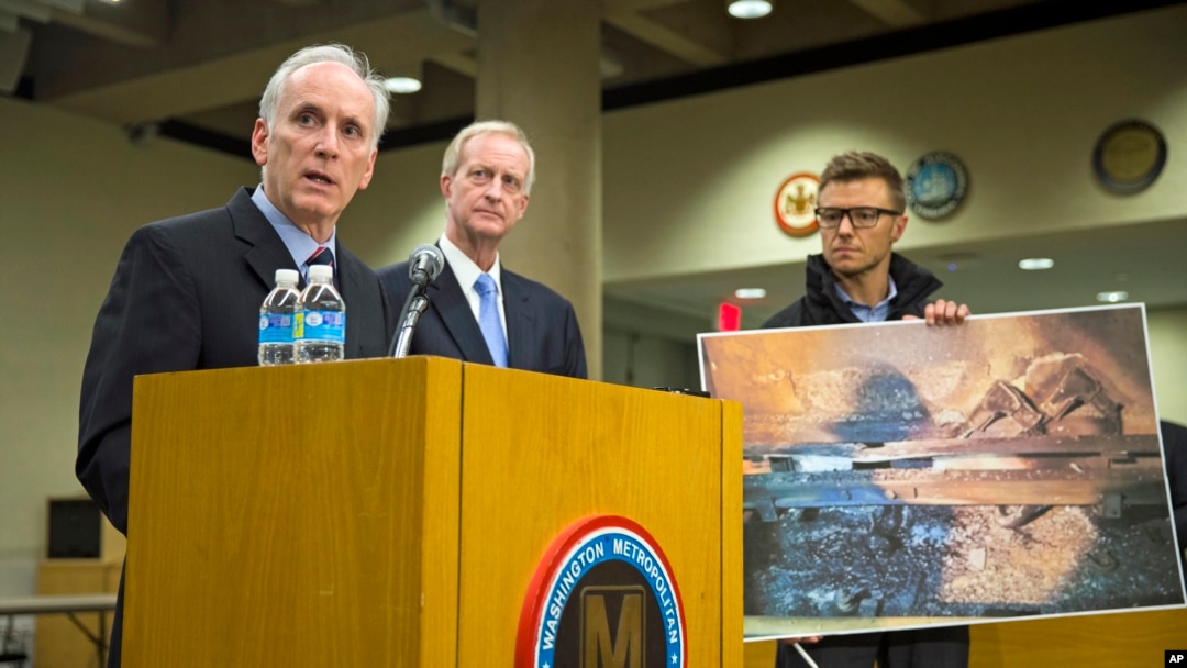An aide to Metro General Manager Paul Wiedefeld (l) holds up a photo of a track damaged by fire as Wiedefeld speaks during a news conference to announce that the DC Metrorail service will be shut down for a full day, at the Washington Metropolitan Area Tr