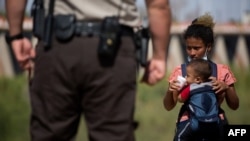 Un migrante de Guatemala le da a beber agua a un bebé mientras espera ser procesado después de entregarse a las autoridades en la frontera entre Estados Unidos y México el 12 de mayo de 2021 en Yuma, Arizona.