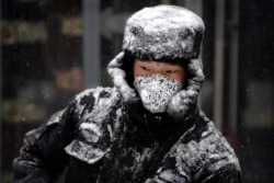 A security guard wears a face mask as he sweeps snow along a pedestrian shopping street during a snowfall in Beijing, Feb. 5, 2020.