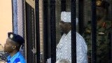 FILE - Sudan's former president Omar Hassan al-Bashir stands guarded inside a cage at the courthouse in Khartoum, Sudan, Aug. 19, 2019.