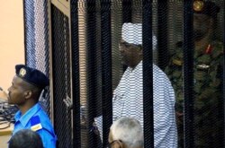 FILE - Sudan's former president Omar Hassan al-Bashir stands guarded inside a cage at the courthouse where he is facing corruption charges, in Khartoum, Sudan, Aug. 19, 2019.