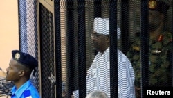 FILE - Sudan's former president Omar al-Bashir stands guarded inside a cage at the courthouse where he is facing corruption charges, in Khartoum, Sudan, Aug. 19, 2019.