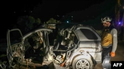 Seorang petugas SAR dari Helm Putih memeriksa bangkai mobil di lokasi serangan udara oleh koalisi AS yang menyasar pemimpin Hurras al-Din, afiliasi Al-Qaeda Suriah, di jalan raya dekat Desa Batabo di barat daya Suriah, Jumat, 31 Januari 2025. (Foto: Abdulaziz Ketaz/AFP)