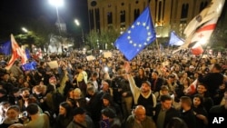 Sejumlah demonstran mengibarkan bendera Uni Eropa dan bendera Georgia dalam aksi protes menentang undang-udang pengaruh asing di luar gedung parlemen di Tbilisi, Georgia, pada 15 April 2024. (Foto: AP/Zurab Tsertsvadze)