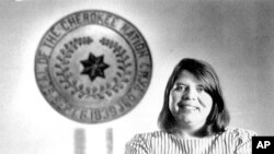 FILE - Wilma Mankiller, the first woman elected chief of the Cherokee Nation, poses in front of the tribal emblem at the Cherokee Nation in Oklahoma, July 19, 1985.