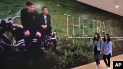 In this March 15, 2018, photo, two women walk past a mural of a Paul Fusco photograph that is part of the exhibit, "The Train: RFK's Last Journey," at the San Francisco Museum of Modern Art in San Francisco.