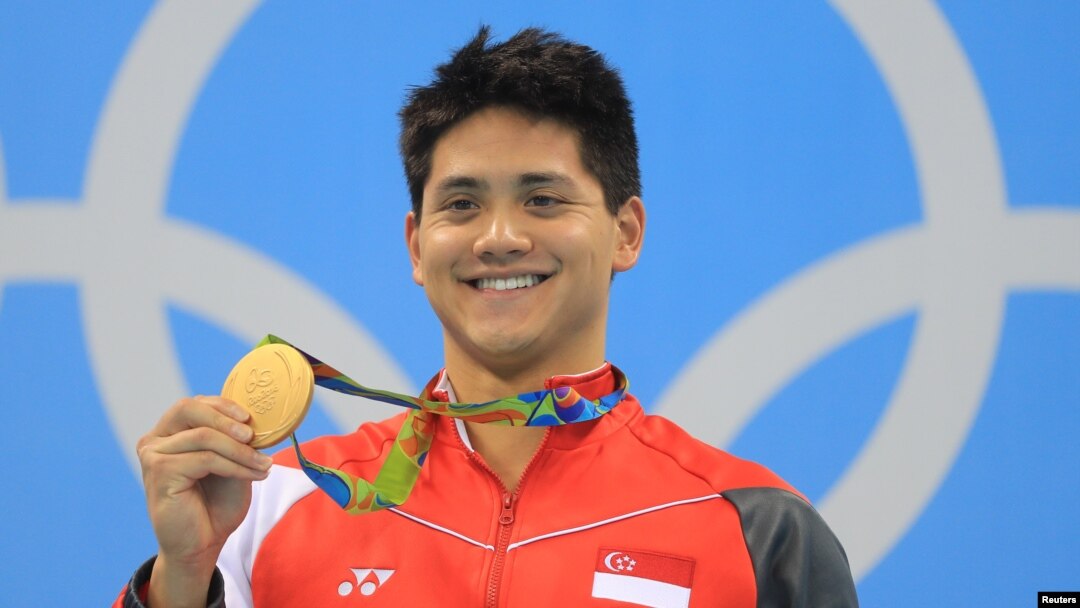 Perenang Singapura, Joseph Schooling, memamerkan medali emas yang diraihnya dalam nomor 100 meter putra gaya kupu-kupu (12/8) di Olimpiade 2016, Rio de Janeiro, Brazil. (Reuters/Dominic Ebenbichler)
