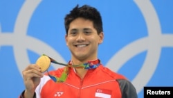 Perenang Singapura, Joseph Schooling, memamerkan medali emas yang diraihnya dalam nomor 100 meter putra gaya kupu-kupu (12/8) di Olimpiade 2016, Rio de Janeiro, Brazil. (Reuters/Dominic Ebenbichler)