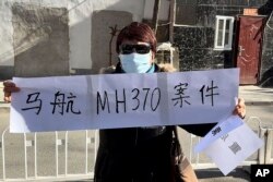 Hu Xiufang, yang putra, menantu, dan cucunya termasuk dalam pesawat MH370 yang hilang, memegang spanduk di Beijing Senin, 27 November 2023. (Foto: AP)