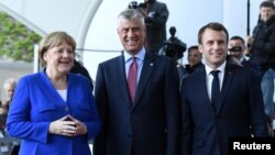 German Chancellor Angela Merkel, left, and French President Emmanuel Macron, right, welcome Kosovo's President Hashim Thaci, center, to a meeting with Western Balkans leaders, at the Chancellery in Berlin, Germany, April 29, 2019.