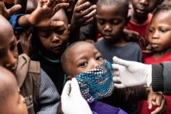 Un niño intenta usar una máscara facial mientras los miembros de la Coalición para los defensores de los derechos humanos de base Kenia (CGHRD'S Kenia) trabajan para su distribución de alimentos.