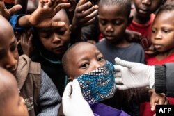 Un niño intenta usar una máscara facial mientras los miembros de la Coalición para los defensores de los derechos humanos de base Kenia (CGHRD'S Kenia) trabajan para su distribución de alimentos.