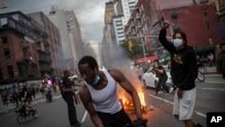 Protesters march down the street as trash burns in the background during a solidarity rally for George Floyd, May 30, 2020, in New York. 