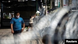 FILE - A migrant worker receives belongings over barbed wire in front of a closed shrimp market, amid the coronavirus disease outbreak, in Samut Sakhon province, in Thailand, Dec. 20, 2020. 