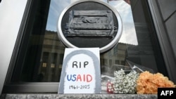 FILE - Tributes are placed beneath the covered seal of the U.S. Agency for International Development (USAID) at its headquarters in Washington, Feb. 7, 2025.