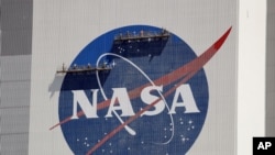 FILE - Workers near the top of the 160-meter Vehicle Assembly Building at the Kennedy Space Center spruce up the NASA logo standing on scaffolds in Cape Canaveral, Fla., in May 2020.