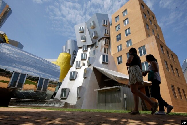 FILE - People walk past the Ray and Maria Stata Center, behind, on the campus of Massachusetts Institute of Technology, in Cambridge, Mass. July 16, 2019. (AP Photo/Steven Senne)