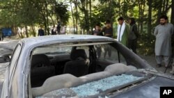 Afghan men look at a damaged car after a roadside bomb explosion in Kabul, Afghanistan, June 6, 2021.