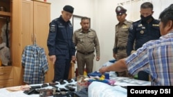 Satu dari tujuh orang yang ditangkap dalam kasus dugaan perdagangan manusia di Thailand, duduk di tempat tidur menunjukkan senjata api yang dimilikinya, Selasa, 15 Desember 2020. (Foto: DSI)