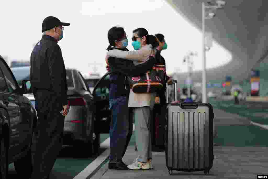 Personas protegidas con tapabocas se abrazan fuera del aeropuerto internacional de Wuhan, tras el levantamiento de las restricciones de viaje que permitió a muchos salir de la ciudad donde comenzó la pandemia que ha puesto en vilo al mundo.